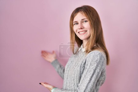 Téléchargez les photos : Belle femme debout sur fond rose invitant à entrer souriant naturel avec la main ouverte - en image libre de droit