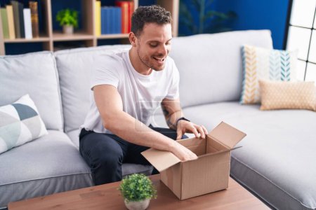 Photo for Young hispanic man smiling confident unpacking cardboard box at home - Royalty Free Image