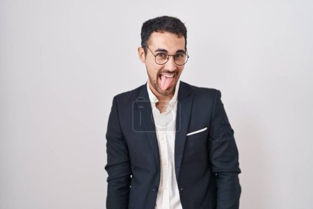 Foto de Hombre hispano de negocios guapo parado sobre fondo blanco sacando la lengua feliz con expresión divertida. concepto de emoción. - Imagen libre de derechos