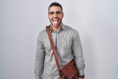 Foto de Un joven hispano con una maleta sacando la lengua feliz con expresión divertida. concepto de emoción. - Imagen libre de derechos