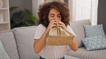 Photo for Young beautiful hispanic woman blowing air on paper bag suffering panic attack at home - Royalty Free Image