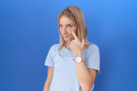 Téléchargez les photos : Jeune femme caucasienne portant un t-shirt bleu décontracté pointant vers l'œil vous regardant geste, expression suspecte - en image libre de droit