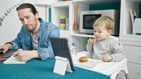 Téléchargez les photos : Père et fils travaillant et prenant soin de l'enfant à la salle à manger - en image libre de droit