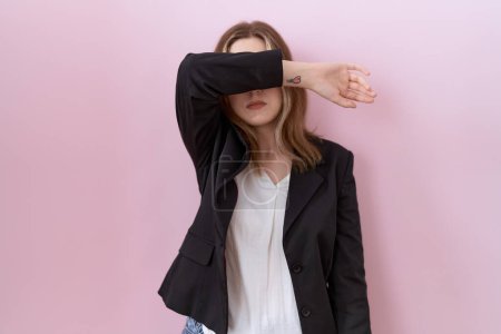 Téléchargez les photos : Jeune femme d'affaires caucasienne portant une veste noire couvrant les yeux avec le bras, l'air grave et triste. concept de non-visibilité, de dissimulation et de rejet - en image libre de droit