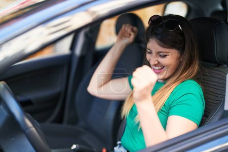 Téléchargez les photos : Jeune femme hispanique assise en voiture dansant dans la rue - en image libre de droit
