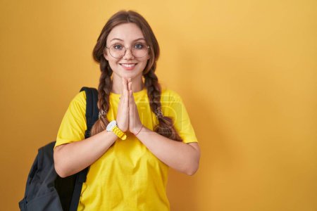 Photo for Young caucasian woman wearing student backpack over yellow background praying with hands together asking for forgiveness smiling confident. - Royalty Free Image
