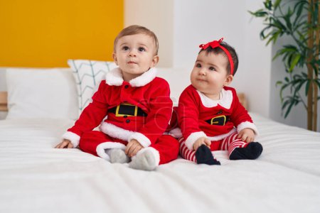 Téléchargez les photos : Adorable garçon et fille portant des vêtements de Noël assis sur le lit dans la chambre - en image libre de droit
