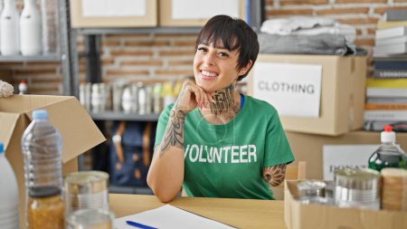 Photo for Hispanic woman with amputee arm volunteer smiling confident sitting on table at charity center - Royalty Free Image