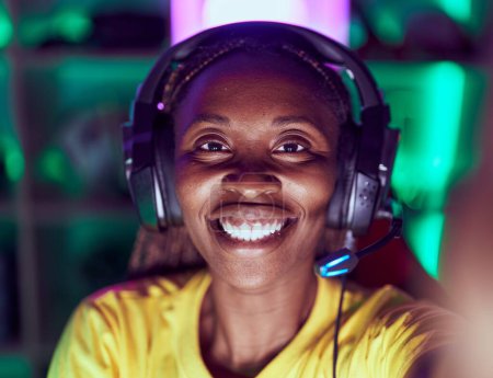 Téléchargez les photos : Afro-américaine femme streamer sourire confiant faire selfie par caméra à salle de jeux - en image libre de droit