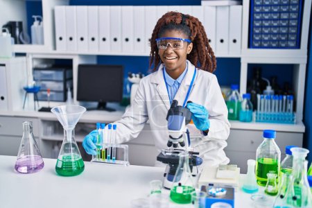 Téléchargez les photos : Femme scientifique afro-américaine utilisant un microscope tenant des éprouvettes en laboratoire - en image libre de droit
