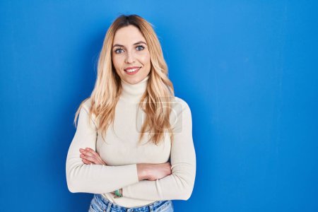 Téléchargez les photos : Young caucasian woman standing over blue background happy face smiling with crossed arms looking at the camera. positive person. - en image libre de droit