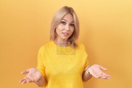 Foto de Mujer caucásica joven con suéter amarillo despistado y confundido con los brazos abiertos, sin concepto de idea. - Imagen libre de derechos