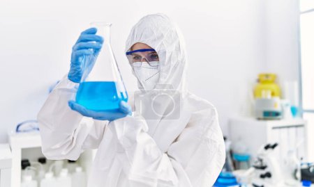 Foto de Joven científica rubia vistiendo uniforme de seguridad sosteniendo tubo de ensayo en laboratorio - Imagen libre de derechos