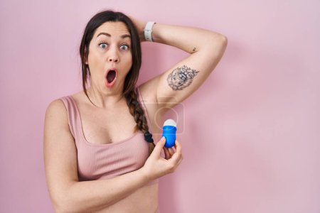 Photo for Young brunette woman using roll on deodorant afraid and shocked with surprise and amazed expression, fear and excited face. - Royalty Free Image