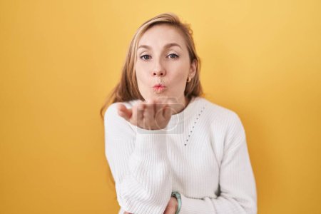 Photo for Young caucasian woman wearing white sweater over yellow background looking at the camera blowing a kiss with hand on air being lovely and sexy. love expression. - Royalty Free Image