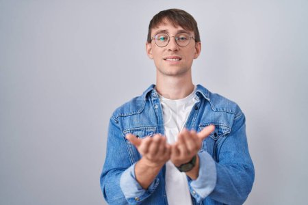 Photo for Caucasian blond man standing wearing glasses smiling with hands palms together receiving or giving gesture. hold and protection - Royalty Free Image