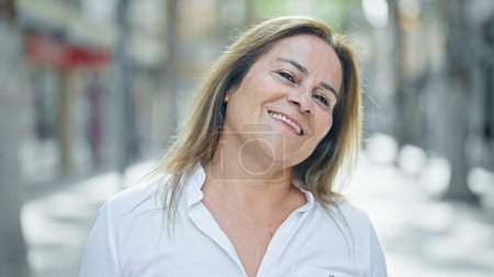 Téléchargez les photos : Moyen Age femme hispanique souriant confiance debout dans la rue - en image libre de droit