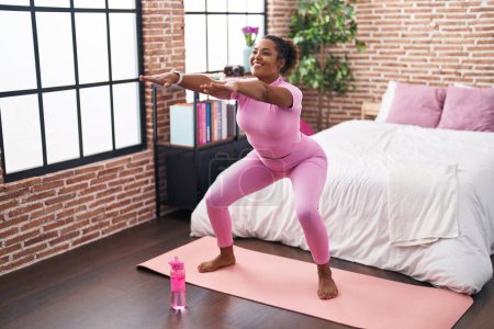 Téléchargez les photos : Femme afro-américaine souriante entraînement confiant exercice de jambe à la chambre - en image libre de droit