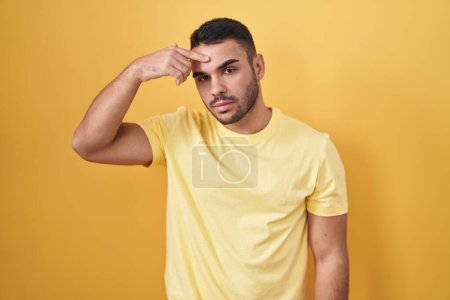 Photo for Young hispanic man standing over yellow background pointing unhappy to pimple on forehead, ugly infection of blackhead. acne and skin problem - Royalty Free Image