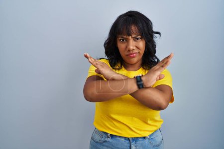 Photo for Hispanic woman standing over blue background rejection expression crossing arms doing negative sign, angry face - Royalty Free Image
