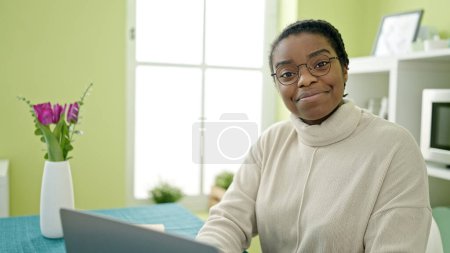 Photo for African american woman using laptop sitting on table at dinning room - Royalty Free Image