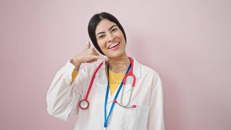Téléchargez les photos : Jeune belle hispanique femme médecin souriant confiant faire appelez-moi geste sur fond rose isolé - en image libre de droit