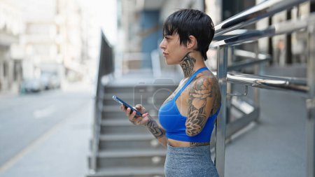 Foto de Mujer hispana con brazo amputado usando smartphone con expresión seria en la calle - Imagen libre de derechos