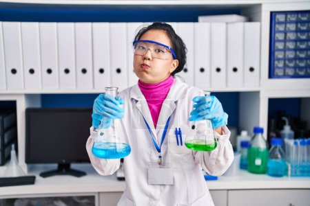 Téléchargez les photos : Jeune femme asiatique travaillant au laboratoire scientifique gonflant les joues avec un visage drôle. bouche gonflée d'air, attrapant l'air. - en image libre de droit