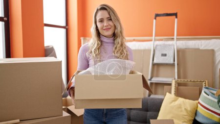 Photo for Young blonde woman smiling confident holding package at new home - Royalty Free Image