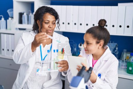 Photo for Mother and daughter scientists holding test tubes writing on notebook at laboratory - Royalty Free Image