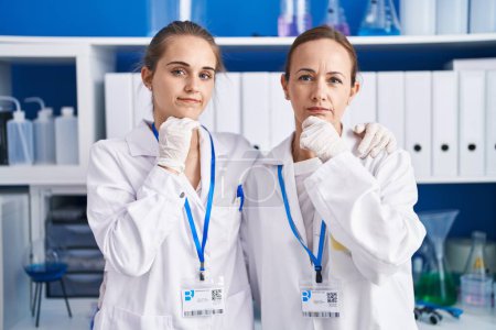 Photo for Two women working at scientist laboratory serious face thinking about question with hand on chin, thoughtful about confusing idea - Royalty Free Image