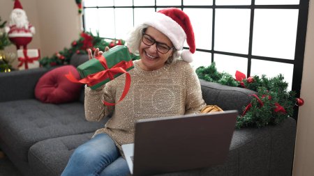 Photo for Middle age woman with grey hair having video call sitting on sofa by christmas tree at home - Royalty Free Image