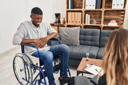 Téléchargez les photos : Homme afro-américain faisant une thérapie assis sur un fauteuil roulant avec la main sur le ventre parce que l'indigestion, la maladie douloureuse se sent mal. concept de douleur. - en image libre de droit