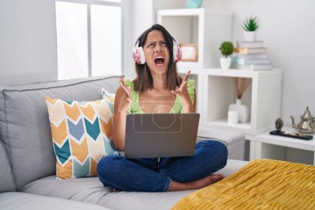 Photo for Hispanic young woman using laptop at home crazy and mad shouting and yelling with aggressive expression and arms raised. frustration concept. - Royalty Free Image