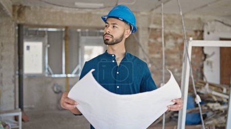 Téléchargez les photos : Jeune architecte hispanique portant un casque dur regardant les plans sur le chantier de construction - en image libre de droit