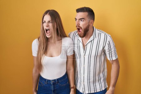 Téléchargez les photos : Jeune couple debout sur fond jaune en colère et fou hurlant frustré et furieux, criant de colère. rage et concept agressif. - en image libre de droit
