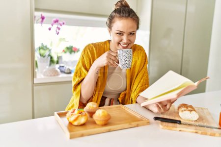 Photo for Young beautiful hispanic woman having breakfast reading book at the kitchen - Royalty Free Image
