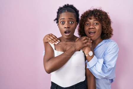 Photo for Two african women standing over pink background afraid and shocked with surprise and amazed expression, fear and excited face. - Royalty Free Image