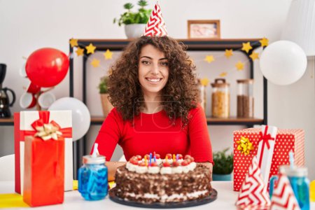 Foto de Mujer hispana con cabello rizado celebrando cumpleaños sosteniendo gran pastel de chocolate luciendo positiva y feliz de pie y sonriendo con una sonrisa confiada mostrando los dientes - Imagen libre de derechos