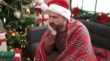 Photo for Young bald man sitting by christmas tree looking upset at home - Royalty Free Image