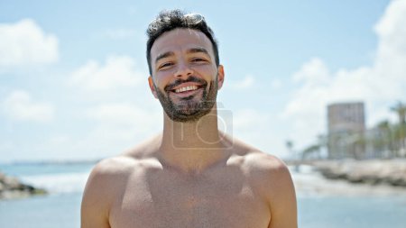 Téléchargez les photos : Jeune homme hispanique touriste souriant confiant torse nu à la plage - en image libre de droit