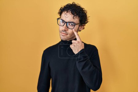 Téléchargez les photos : Hispanic man standing over yellow background pointing to the eye watching you gesture, suspicious expression - en image libre de droit