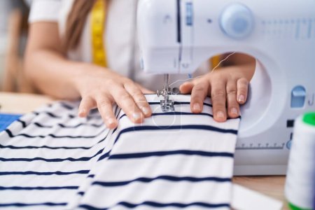 Photo for Young beautiful hispanic woman tailor using sewing machine at clothing factory - Royalty Free Image