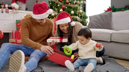 Photo for Couple and son unpacking gift sitting on floor by christmas tree at home - Royalty Free Image
