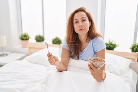 Foto de Mujer morena desayunando en la cama relajada con expresión seria en la cara. simple y natural mirando a la cámara. - Imagen libre de derechos