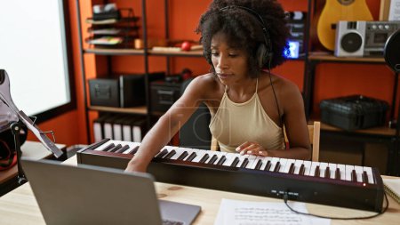 Photo for African american woman musician playing piano using laptop at music studio - Royalty Free Image