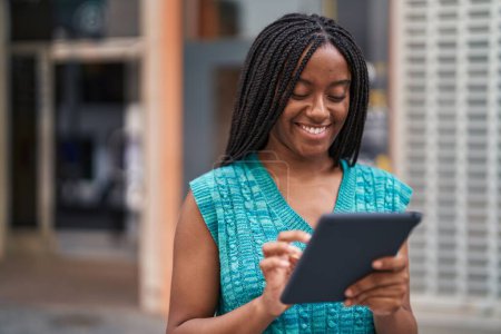 Téléchargez les photos : Afro-américaine femme souriant confiant en utilisant touchpad à la rue - en image libre de droit