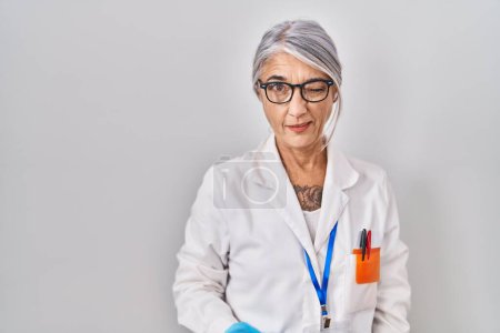 Téléchargez les photos : Femme d'âge moyen avec les cheveux gris portant robe scientifique clin d'oeil en regardant la caméra avec une expression sexy, gai et heureux visage. - en image libre de droit