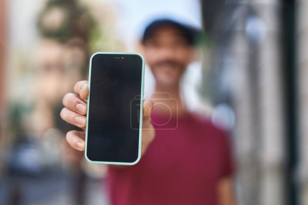Foto de Joven hombre hispano sonriendo confiado mostrando aplicación de smartphone en la calle - Imagen libre de derechos
