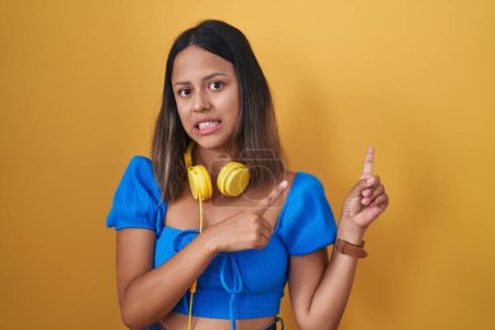 Téléchargez les photos : Jeune femme hispanique debout sur fond jaune pointant de côté inquiet et nerveux avec les deux mains, préoccupé et expression surprise - en image libre de droit